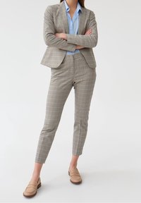 Costume à carreaux gris avec un blazer ajusté et un pantalon sur mesure. Chemise bleu clair en dessous. Mocassins beiges complètent la tenue. Texture lisse.