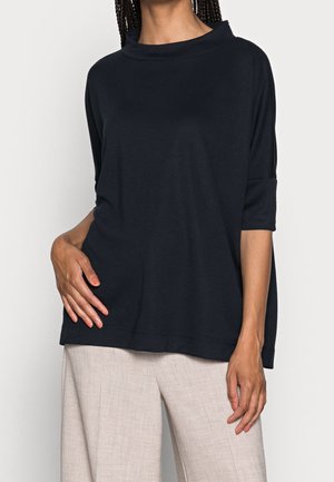 Top blu navy ampia e morbida, con ampio colletto e maniche a tre quarti, abbinato a pantaloni beige chiaro.