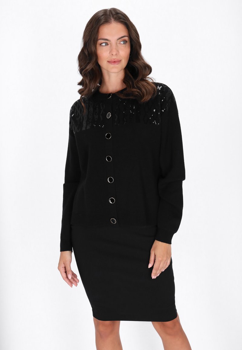 Cardigan negru cu un top texturat din paiete și nasturi mari argintii, asortat cu o fustă creion neagră. Material moale, mâneci lungi.
