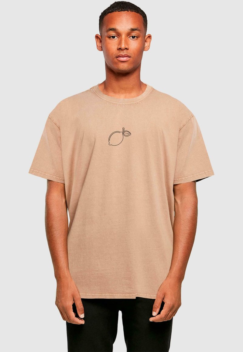 En oversized t-shirt i tan lavet af bomuld, med en sort omridset citron-tryk på brystet. Korte ærmer og rund hals.