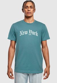 Türkis puuvillane T-särk, millel on valge gooti kiri "New York". Lühikesed varrukad ja vaba lõige, millel on sile tekstuur.