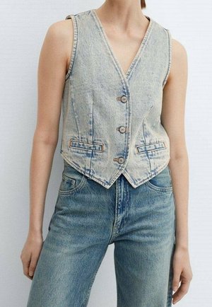 Woman wearing light blue sleeveless denim vest with buttons and matching high-waist blue denim jeans against plain background.