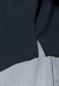 Tmavě námořnická texturovaná tkanina s mírným vlnitým vzorem, s bočním rozparkem, vrstvená přes světle pruhovanou tkaninu.