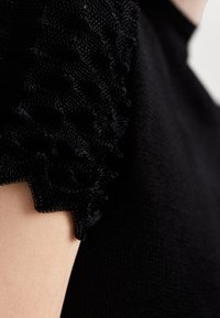 Sort striktop med strukturerede puffærmer i honningkakes mønster. Den glatte stofkvalitet på kroppen står i kontrast til det hævede ærmedesign.