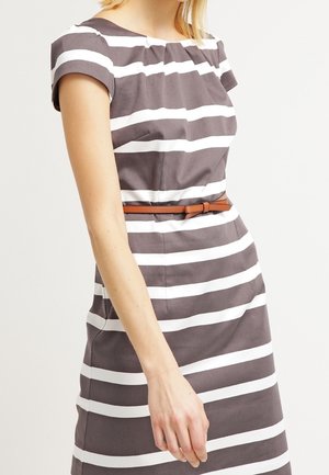 Femme portant une robe à rayures horizontales grises et blanches avec des manches courtes et une fine ceinture marron à la taille, sur un fond uni.