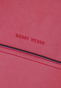 Różowa skórzana tekstura z wytłoczonym logo "GERRY WEBER"; wyróżnia się niebieskim akcentem w szwie dla dodatkowego detalu.