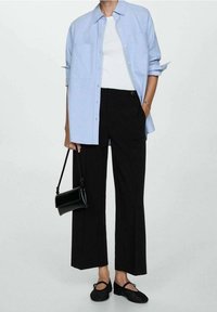 Lichtblauw overhemd, witte t-shirt, zwarte wijde broek, zwarte crossbody tas en zwarte flats met een strapdetail.