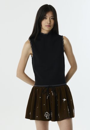 Haut noir sans manches avec col montant, accents en clous argentés sur les épaules, associé à une jupe marron ornée de motifs floraux et d'une taille à cordon.
