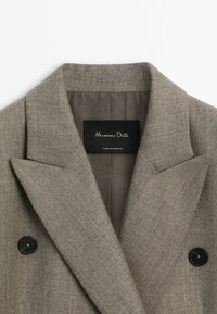 Blazer gris croisé avec larges revers et boutons noirs, montrant l'étiquette intérieure "Massimo Dutti Made in Portugal."