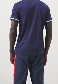 Námořnické sportovní tričko s bílými pruhy na rukávech, vyrobené z hladké tkaniny; kombinované s námořnickými kalhotami s červenými bočními pruhy.