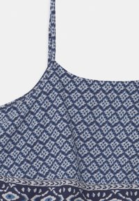 Blue patterned camisole featuring a geometric design, with thin straps and a textured fabric, transitioning to a contrasting border.