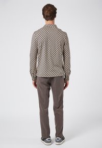 Langsleeve shirt met een geometrisch patroon in beige, bruin en marineblauw; gecombineerd met grijze broeken; achteraanzicht toont een eenvoudige stijl en een slim fit.