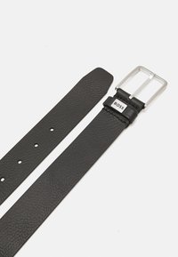 Ceinture en cuir noir avec une finition texturée, dotée d'une boucle en métal argenté et d'un accent de logo. Comprend plusieurs trous d'ajustement.