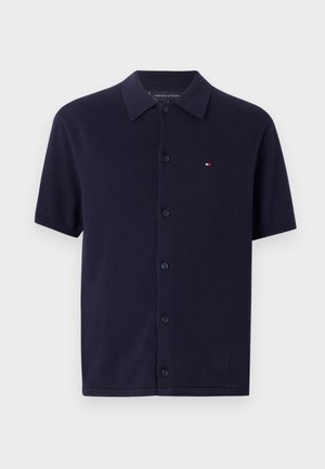 Kortärmad marinblå pikétröja i bomull, med knappstängning fram och en liten broderad logotyp på vänster bröst.
