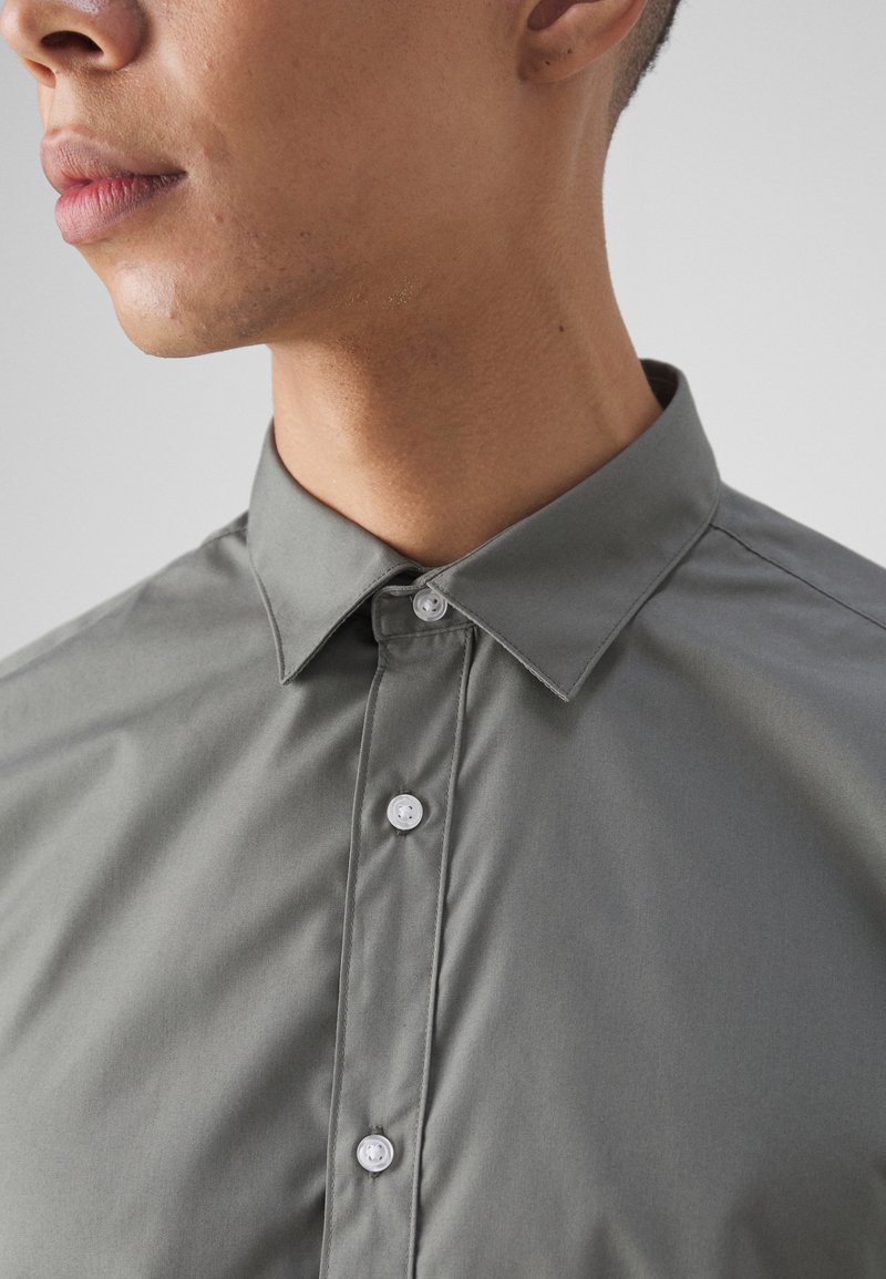 Grauhemd mit klassischem Kragen, das eine glatte Textur aufweist und über weiße Knöpfe entlang der Knopfleiste verfügt. Nahansicht des Halsausschnitts.