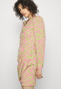 Vestido curto rosa e verde com padrão de corações, mangas longas e detalhe franzido de lado. Feito de um tecido leve e suave.