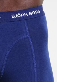 Sötétkék boxer alsónadrág, fehér elasztikus derékkal, amelyen a "BJÖRN BORG" felirat található, sima felülettel és megerősített varrási részletekkel.