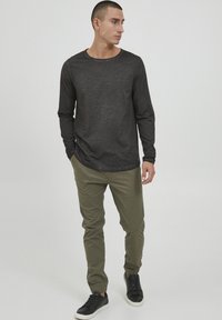 Langærmet skjorte i kulgrå med en struktureret overflade, parret med olivengrønne tapered bukser og sorte sneakers med hvide såler.