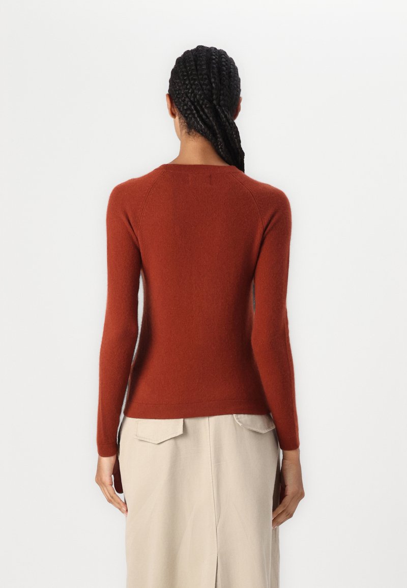Sweter z długim rękawem o prążkowanej strukturze w kolorze rdzy, wykonany z miękkiego materiału dzianinowego. Posiada zaokrąglony dekolt oraz dopasowany fason. Prosty design, bez wzorów.
