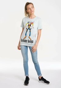 Light blue cotton t-shirt featuring a colorful cartoon character design, with black text "LUCKY LUKE" at the bottom. Styled with skinny jeans.