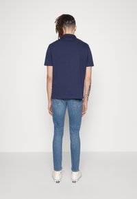 Marinblå piké med korta ärmar, i bomull, rak skärning. Ljusblå jeans, slim fit, med urtvättad textur, kombinerat med vita canvas sneakers.