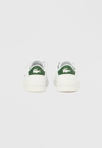 Λευκά αθλητικά παπούτσια με πράσινες λεπτομέρειες στη φτέρνα, λείο δερμάτινο υλικό, χαμηλή σχεδίαση με υφή στη σόλα και λογότυπο.