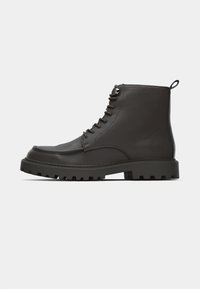 Bruna läderankelboots med strukturerad yta, snörningsdesign och en robust sula med djupa spår för grepp. Förstärkt tå och häl.