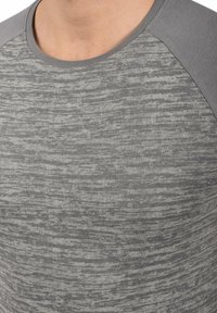 Camiseta gris con un patrón texturizado, con cuello redondo y mangas raglán en un tono gris sólido. Tejido suave con un ligero brillo.