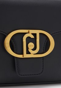 Fermoir de sac en cuir noir avec une boucle ovale dorée présentant les lettres entrelacées "L" et "J" et "LIU·JO" gravé au centre.