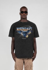 Svart oversized t-skjorte med ørn grafikk og flerfarget tekst. Bomullsstoff, rund hals, korte ermer, enkel design.
