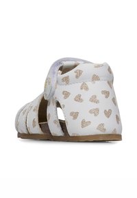 Sandalia blanca con patrones de corazones dorados, diseño abierto, correa de velcro y suela texturizada. Presenta cortes para transpiración.