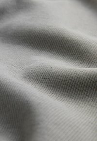 Helle graue Stoff mit einer gerippten Textur, der weiche, fließende Falten und subtile Variationen in der Oberflächendetailierung aufweist.