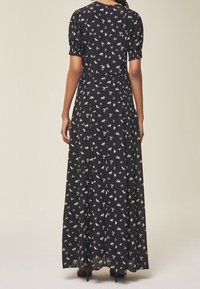 Svart blomster maxi-klänning med korta puffärmar, cinchad midja och ett flödande, lätt tyg med små blommönster genomgående.