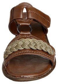 Sandale en cuir brun avec un accent en textile tressé vert. Elle présente une large lanière et un détail en métal circulaire, un design ouvert à l'avant et une semelle plate.