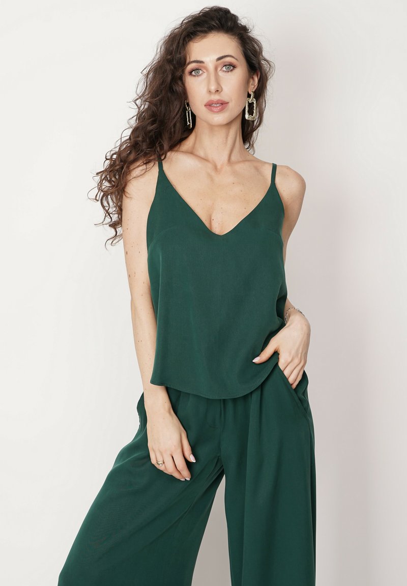 Szmaragdowozielony, lekki top na ramiączkach z dekoltem w kształcie V, w zestawieniu z luźnymi, dopasowanymi spodniami z bocznymi kieszeniami.