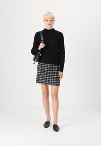 Must deriga must varras, millel on kõrge kaelus, koos musta ja valge ruudulisest tweed seelikuga. Mustad lamedad kingad ja õlal kantav kott.