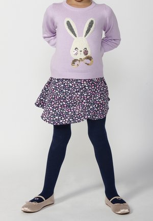 Lichtpaarse trui met een konijn-graphic, gelaagde bloemenrok in marineblauw en roze, marineblauwe panty’s en beige ballerina's met een strik.