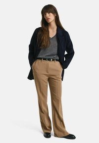 Navy blazer, gray V-neck sweater, and khaki wide-leg trousers; the outfit features a gold belt buckle and black shoes. Smooth fabric texture.