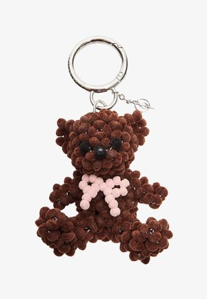 Porte-clés en forme d'ours en peluche marron fabriqué à partir de pompons texturés, avec des yeux en plastique noir et un nœud rose clair. Anneau en métal pour fixation.