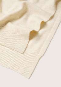 Tissu tricoté doux de couleur crème avec bords côtelés, plié pour montrer la texture et l'élasticité du matériau.