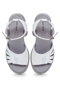 Sandales blanches avec un dessus en cuir lisse, design ouvert sur l'avant et une sangle à la cheville. Présentent des découpes et une semelle intérieure rembourrée grise.