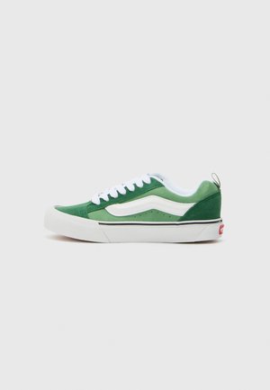 Green suede sneaker with white accents, round toe, flat white sole, classic design, and a small red logo at the heel.