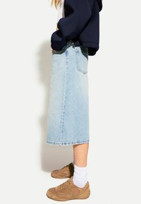 Riflová sukně světle modré barvy s délkou ke kolenům, rovného střihu, s třepeným lemem a zadními kapsami. Nošena s hnědými teniskami a bílými ponožkami.