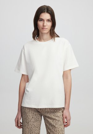 T-shirt en coton blanc à manches courtes, col rond, coupe décontractée, texture lisse, associé à un pantalon beige à motifs.