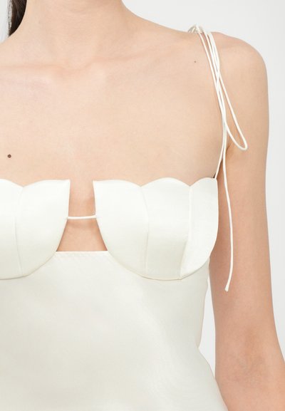 Vestido de satén blanco con escote ondulado y tirantes finos. Textura suave con una silueta ajustada y detalle recortado en el pecho.