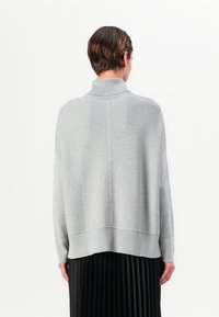 Lys grå genser med høy krage, ribbestrikkede mansjetter og kant. Designet har en løs passform og er laget av mykt strikket stoff.