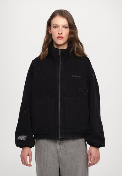 Sort lynlåsjakke med høj krave, der har teksturerede krydsdesigns og to forlommer. Elastiske ærmekanter og kant forneden. Denimstof.