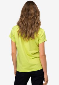 T-shirt di cotone giallo neon con maniche corte, una vestibilità comoda e una texture liscia, indossato con pantaloni in denim scuri.