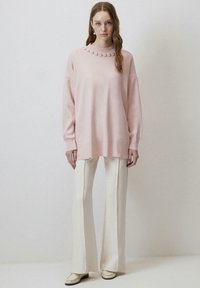 Pulover oversized roz cu guler striat, decorat cu perle, asortat cu pantaloni evazați albi și loafers de culoare deschisă.