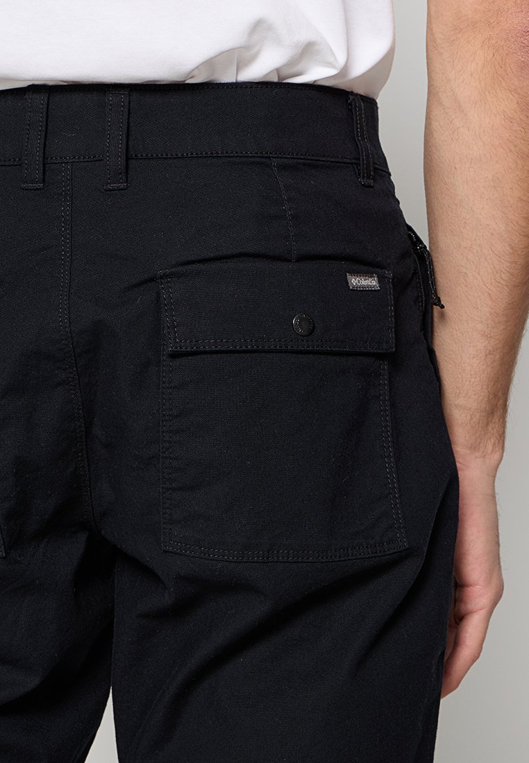 Schwarze Hosen aus strapazierfähigem Material mit einer hinteren aufgesetzten Tasche, Knopfdetails und einem kleinen Markenetikett auf der oberen rechten Tasche.